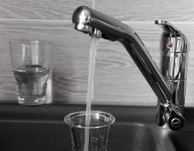 Faucet pouring water into a glass in a kitchen sink; another glass sits to the left, partially filled.