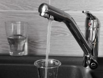 Faucet pouring water into a glass, another glass is partially filled beside it; a kitchen sink is in the background.