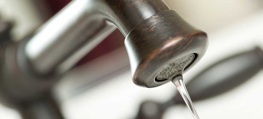 Contact Plumbworks for Faucet installation and repair. Close-up of a bronze faucet with water flowing out.