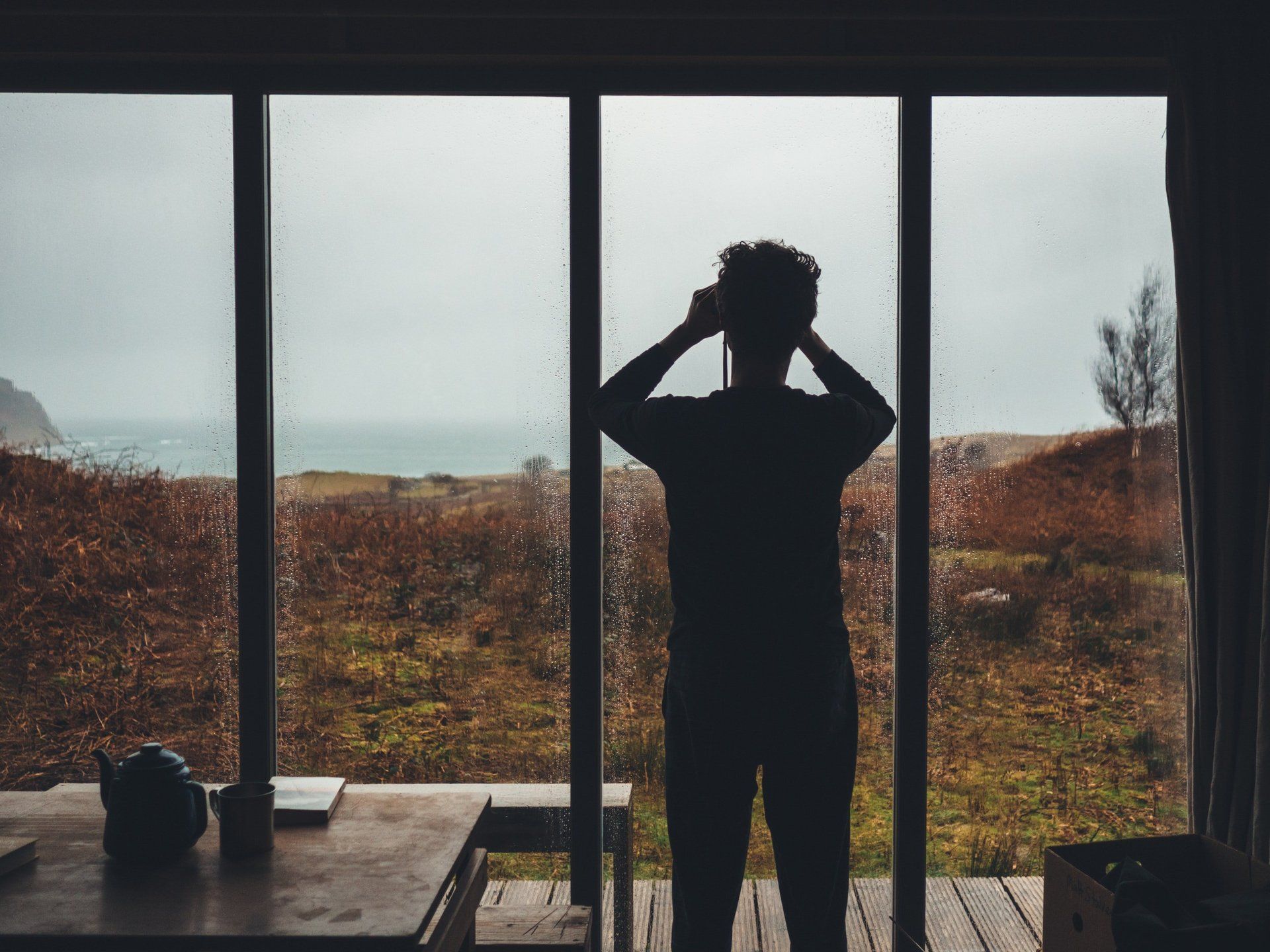 A man is standing in front of a window with his hands on his head.