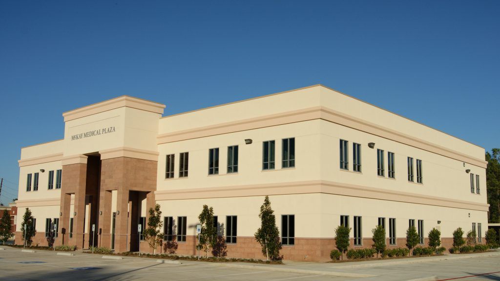 Two-story beige building with brick accents and many windows under a clear blue sky.