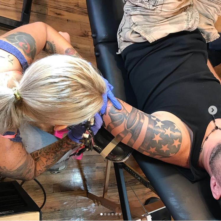 Tattoo artist tattooing a client’s arm on a black chair, close-up overhead view.