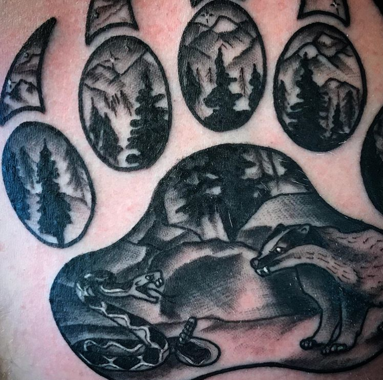 Black-and-gray tattoo of a mountain scene with pine trees, a bear, and a wolf under the moon