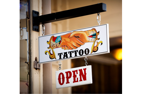 Tattoo shop sign with flaming skull art and a red OPEN sign hanging below