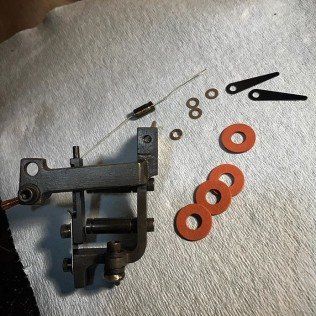 Small metal mechanical parts laid out on a white cloth, including rings, washers, and black levers.