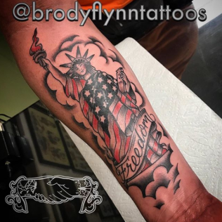 Arm tattoo of a bald eagle with a U.S. flag and the word “Freedom” in black and red ink