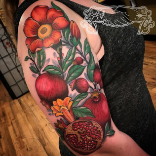 Colorful floral-and-pomegranate tattoo on an upper arm