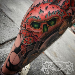 Red skull tattoo on a lower leg, with black and green eyes and red floral details.