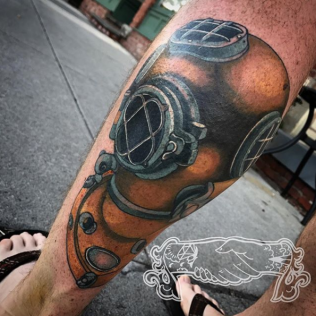 Close-up of a leg tattoo featuring a vintage diving helmet in orange and black ink