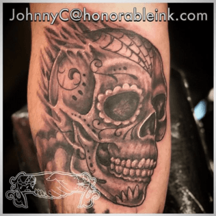 Black-and-gray skull tattoo with floral swirls on a forearm