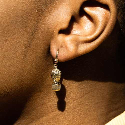 Close-up of an ear wearing a dangling gold earring on dark skin.