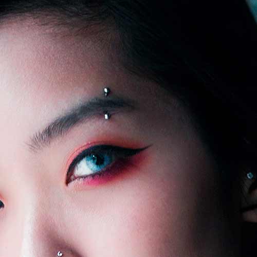 Close-up of a face with bright blue eye makeup and a silver eyebrow piercing