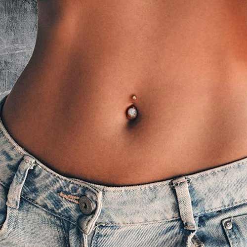 Close-up of a bare midriff with a navel piercing above light blue jeans