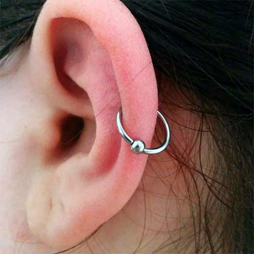 Close-up of a pink ear with a silver hoop piercing and small ball charm