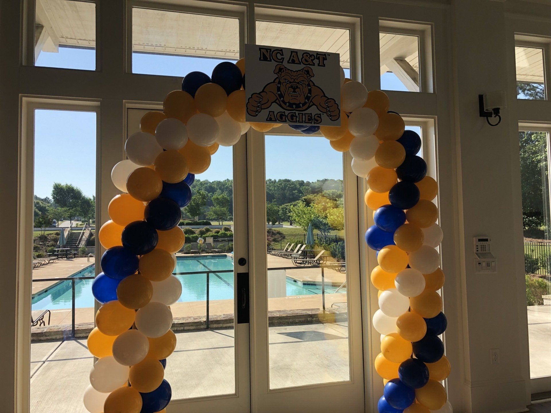 Blue, white, and gold balloon arch framing a doorway inside a venue overlooking a pool