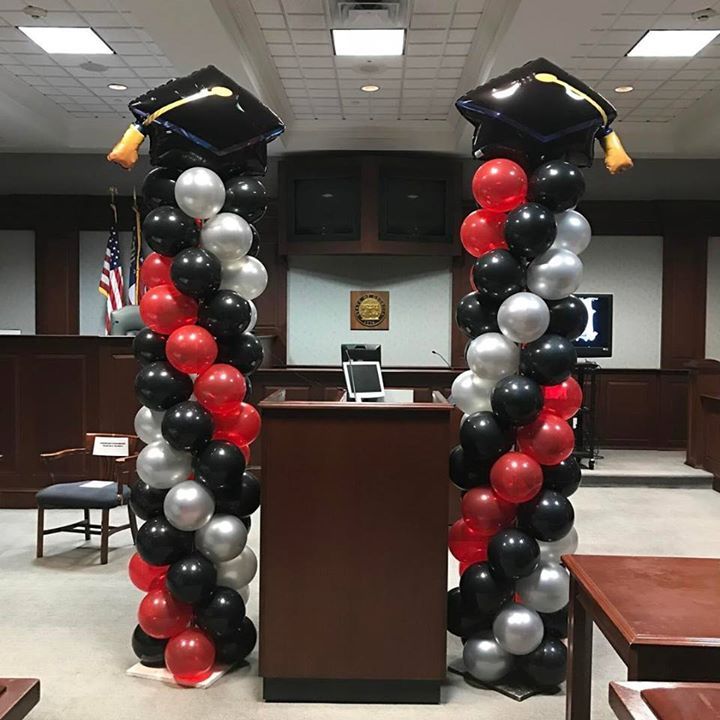 Red, black and silver balloons in a spiral design topped with a square academic cap are placed on either side of a podium.