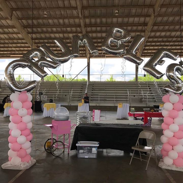 Two pink and white balloon columns act as anchors for a letter archway spelling 