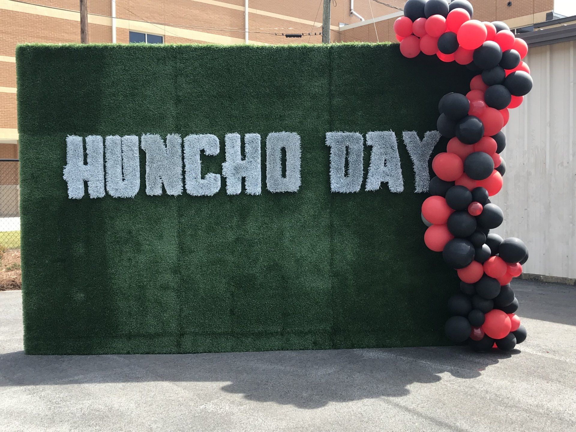 A Huncho Day Grass Wall with a black and red balloon garland.