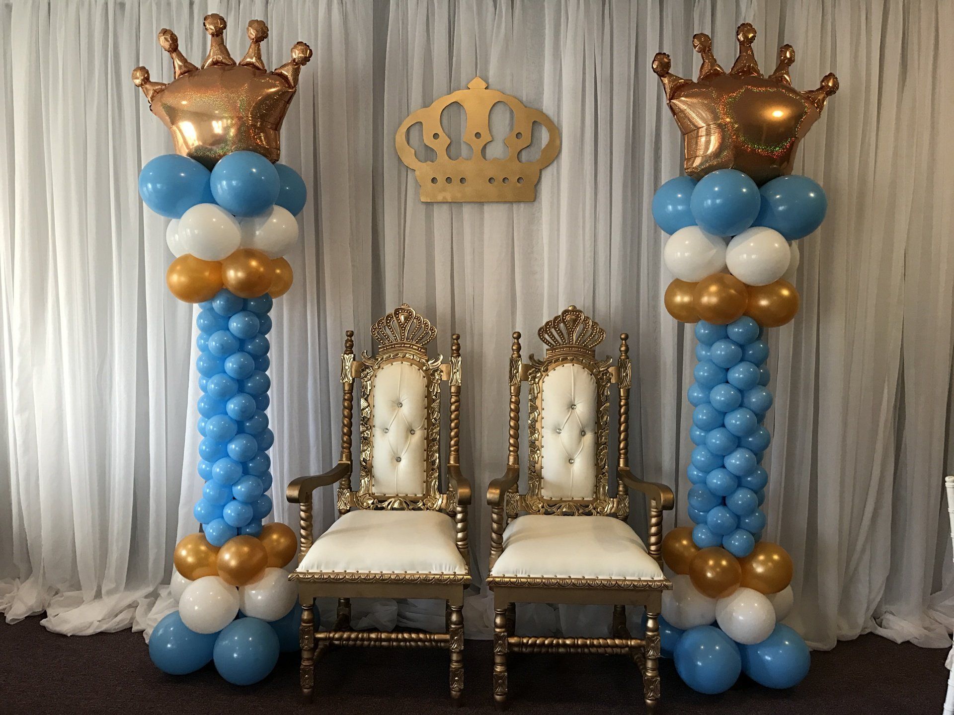 Two grand columns comprised of baby blue, white and gold with crowns at the top sit on either site of two thrones.