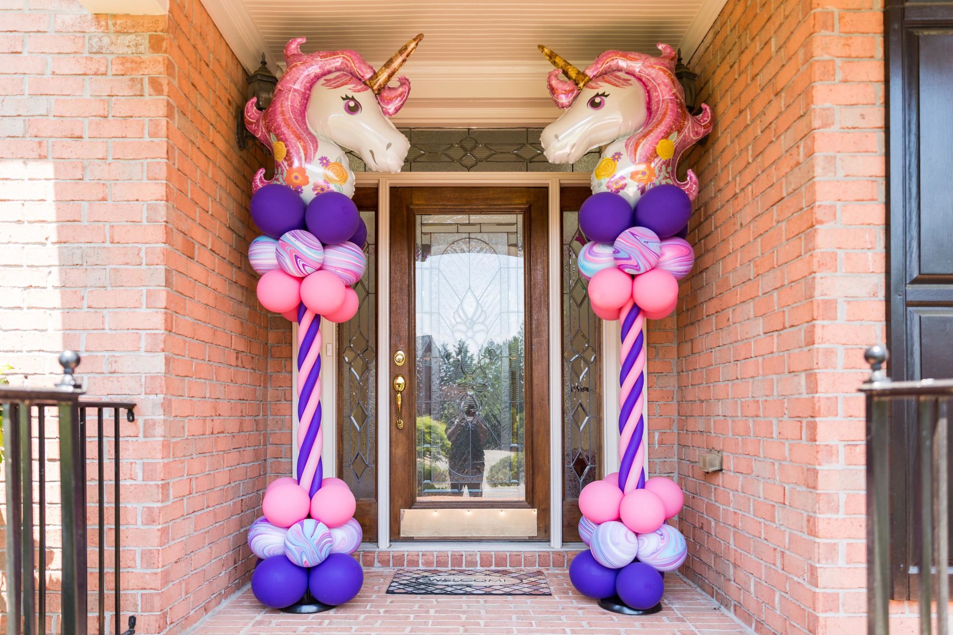 Unicorn themed first birthday balloon columns with pastel balloons and character toppers framing front door entrance