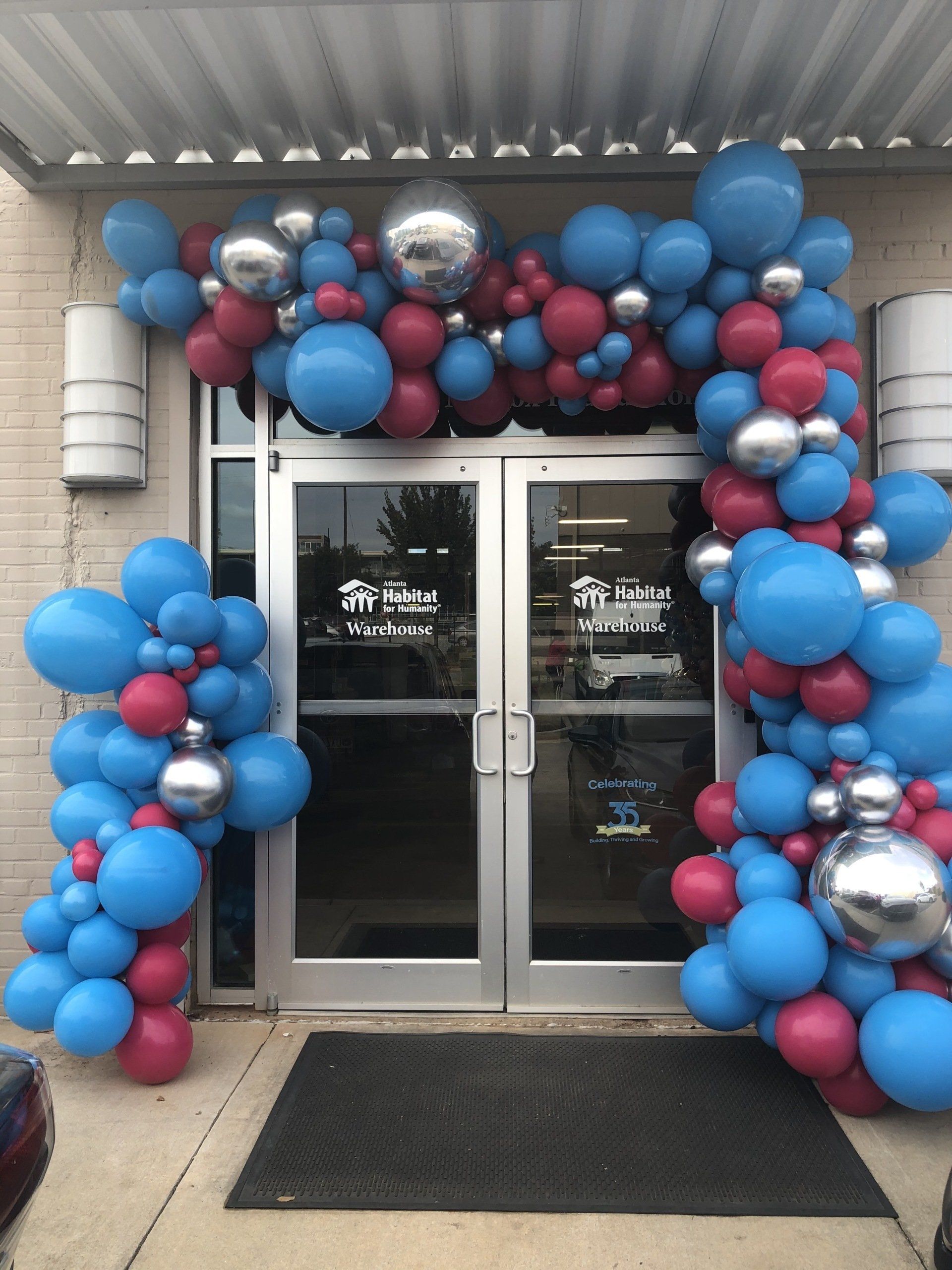 Blue pink and silver balloon garland above storefront entrance with oversized chrome balloons