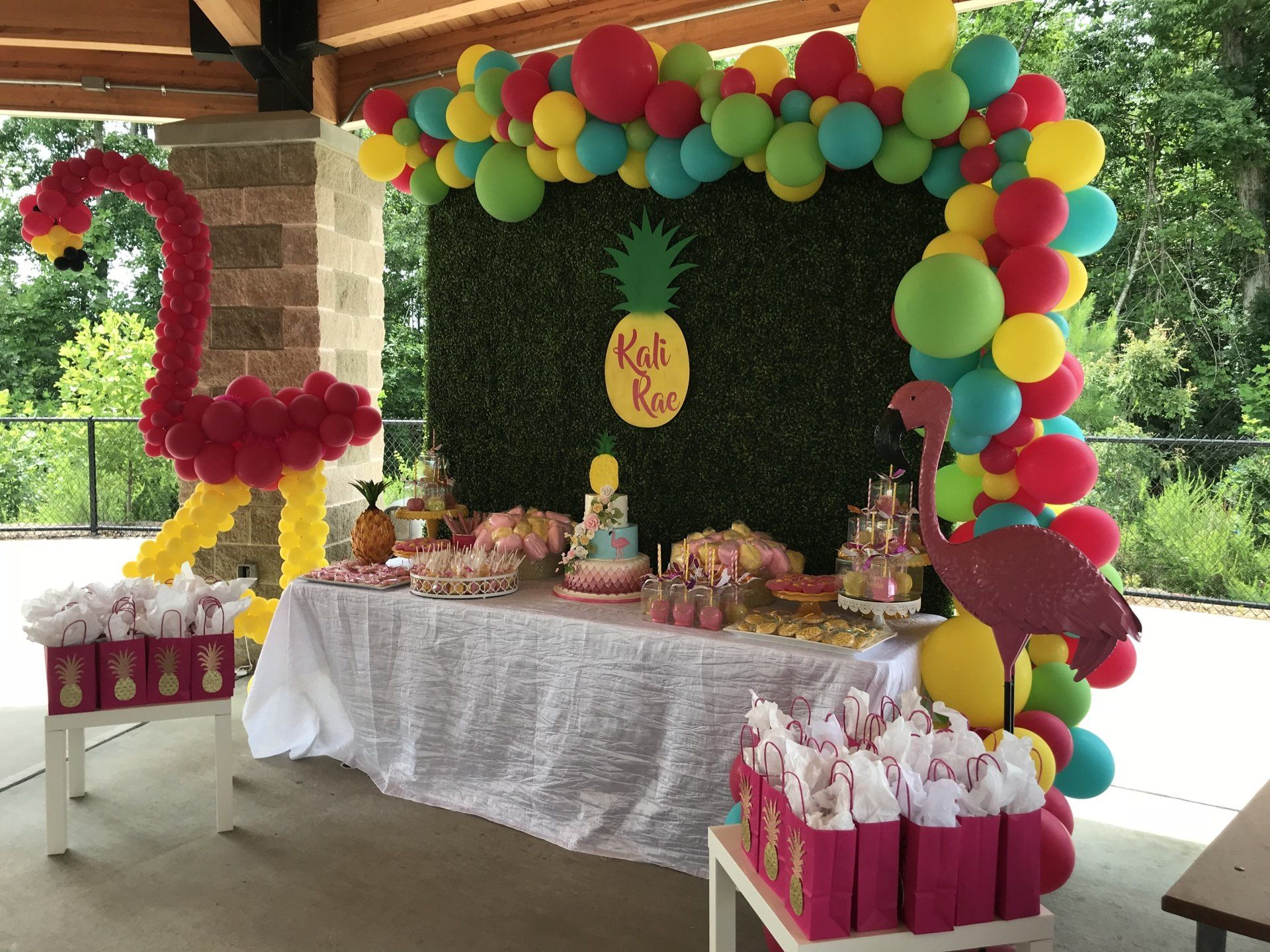 A tropical themed dessert table with a grass wall and an organic balloon garland.