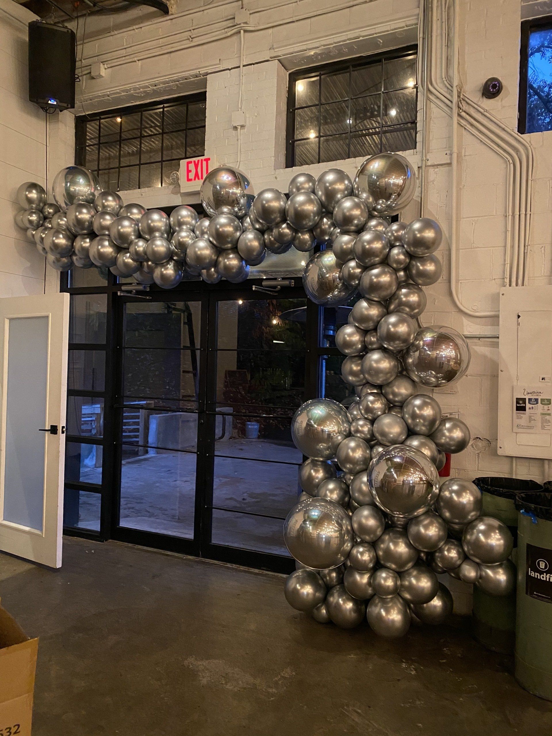 Metallic silver chrome balloon garland installed along industrial wall for modern event entrance