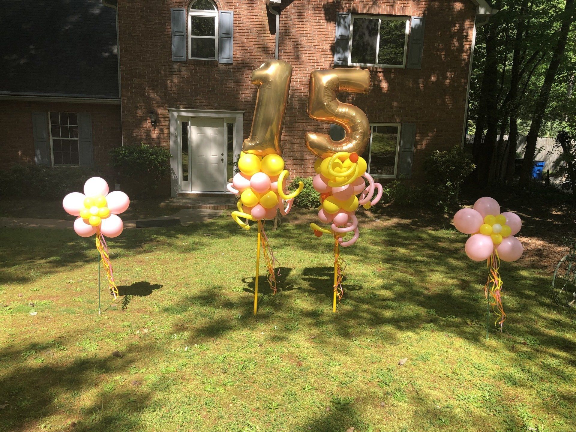 Gold number fifteen balloons with balloon flower accents arranged across front yard for outdoor birthday decor