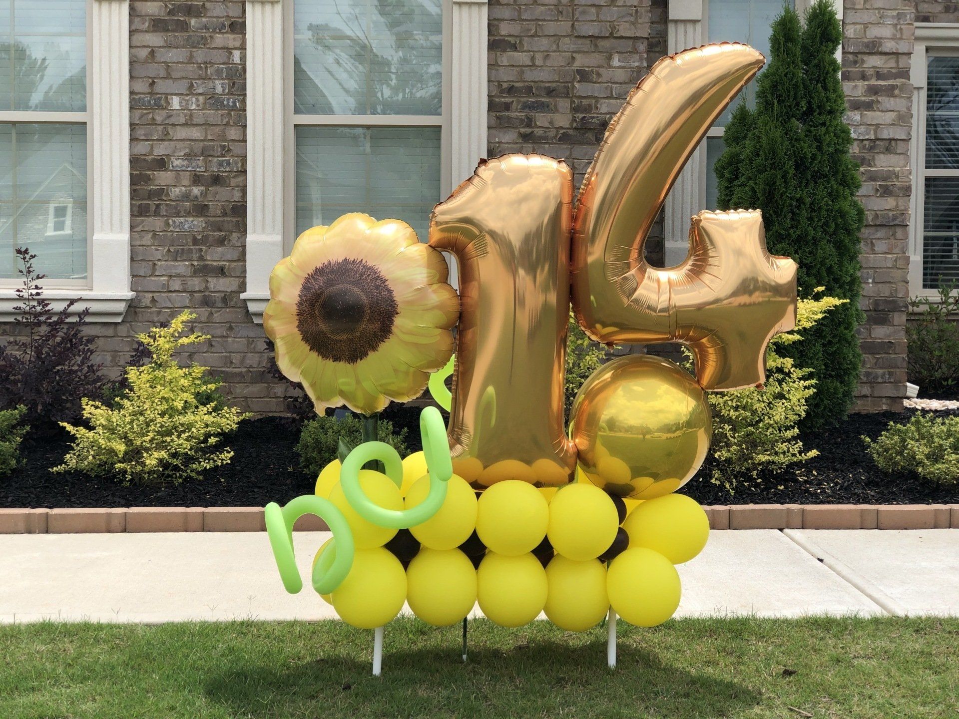 Gold number sixteen balloon sculpture with sunflower theme and yellow balloon base for sweet sixteen party