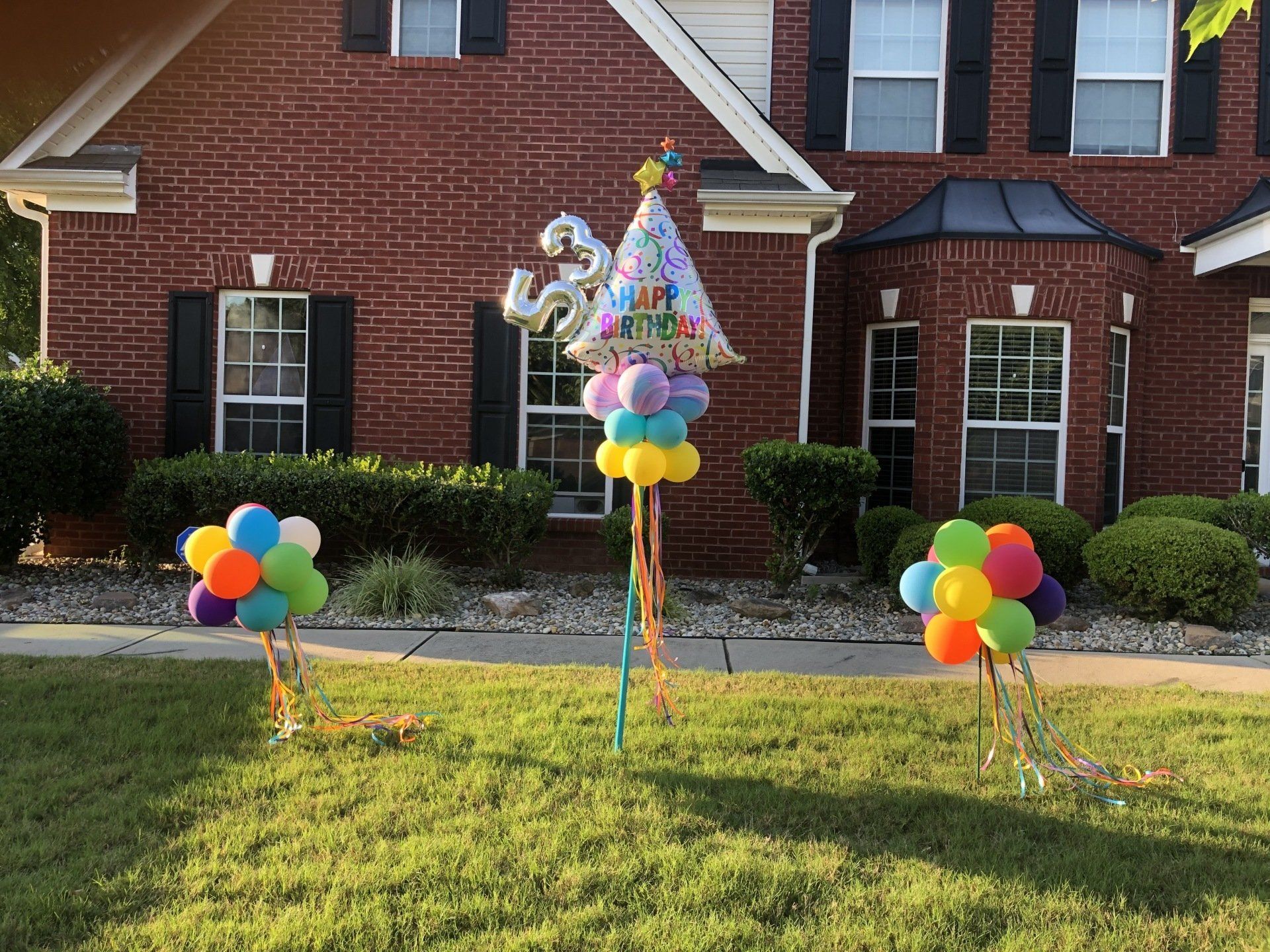Colorful birthday balloon yard sign and clusters placed in front of brick home for outdoor party