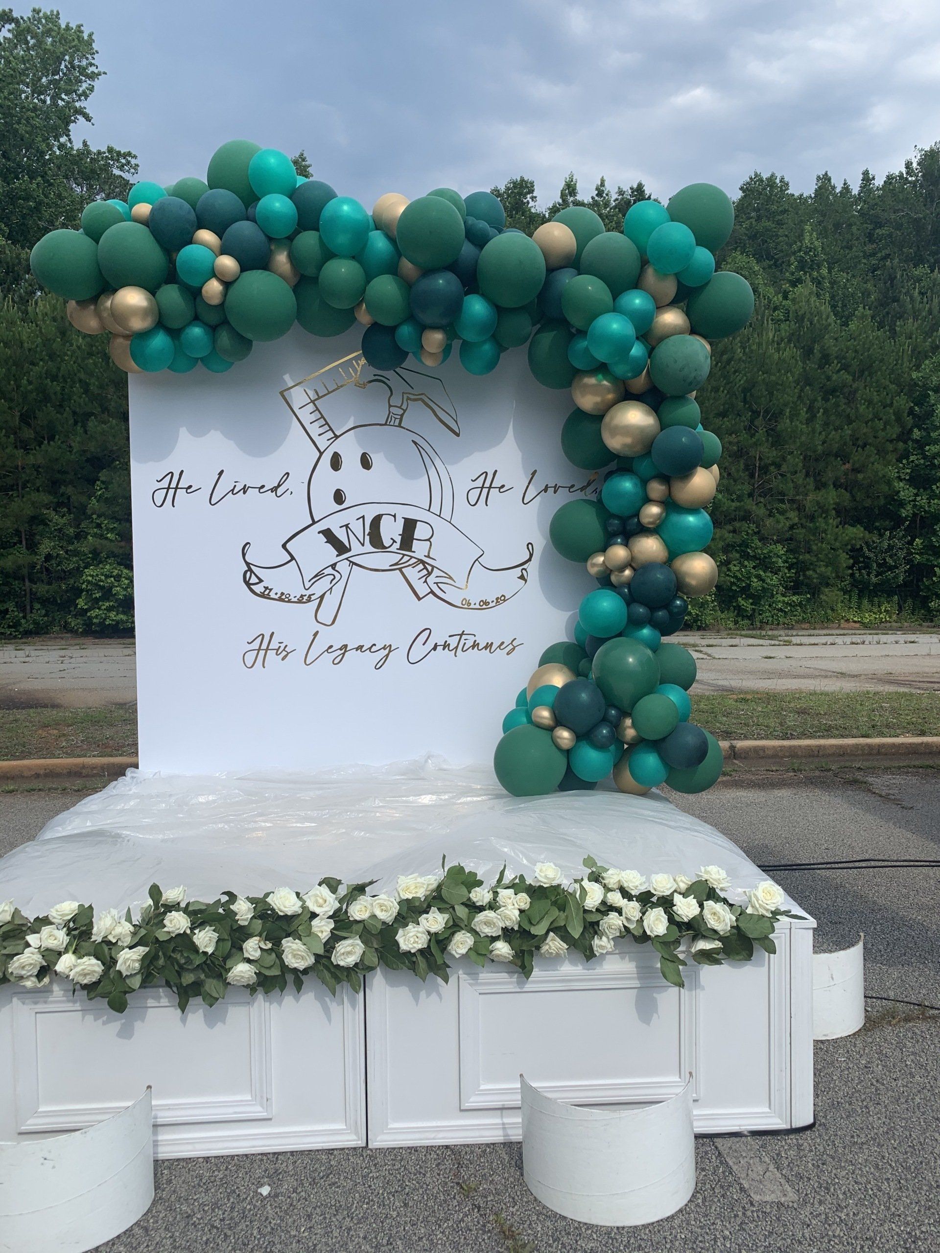 Green and gold organic balloon arch over outdoor branded backdrop for corporate or community event
