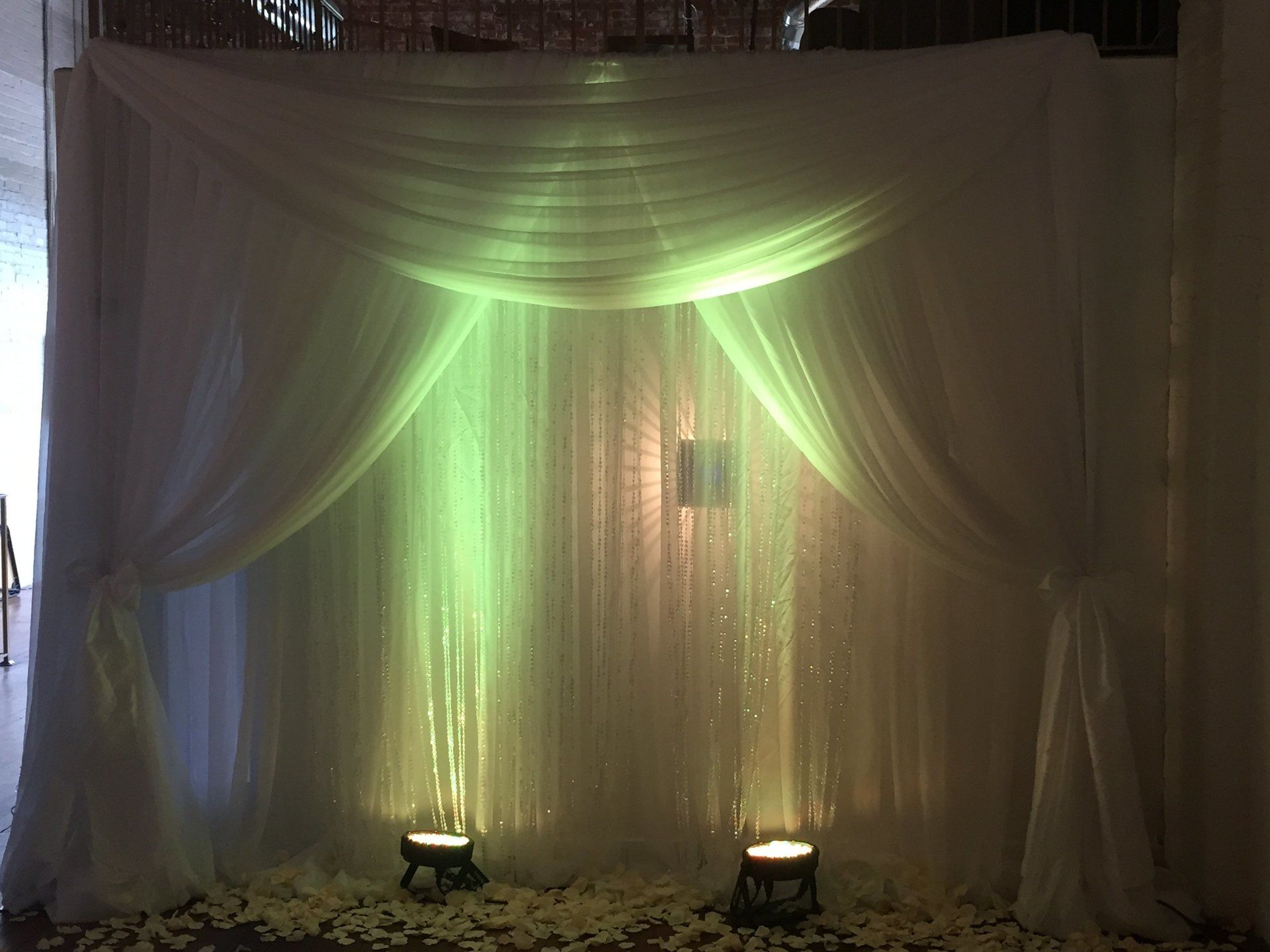 White draped backdrop with soft uplighting for wedding ceremony or reception stage