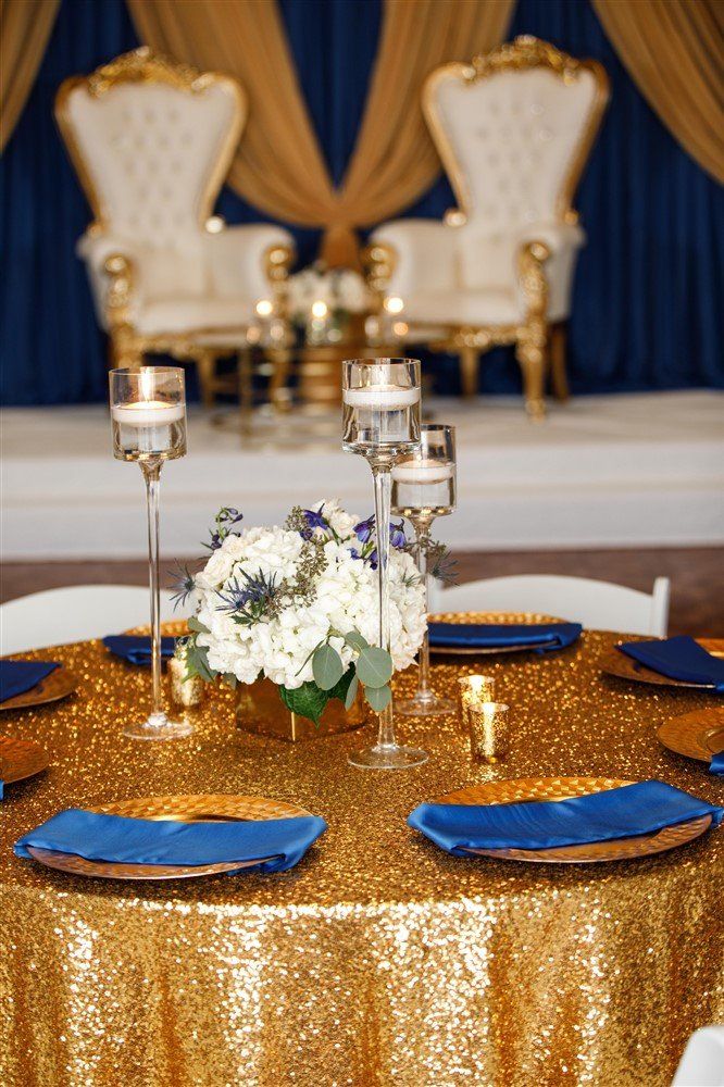Royal blue and gold draped backdrop with white throne chairs and candle décor for a formal event