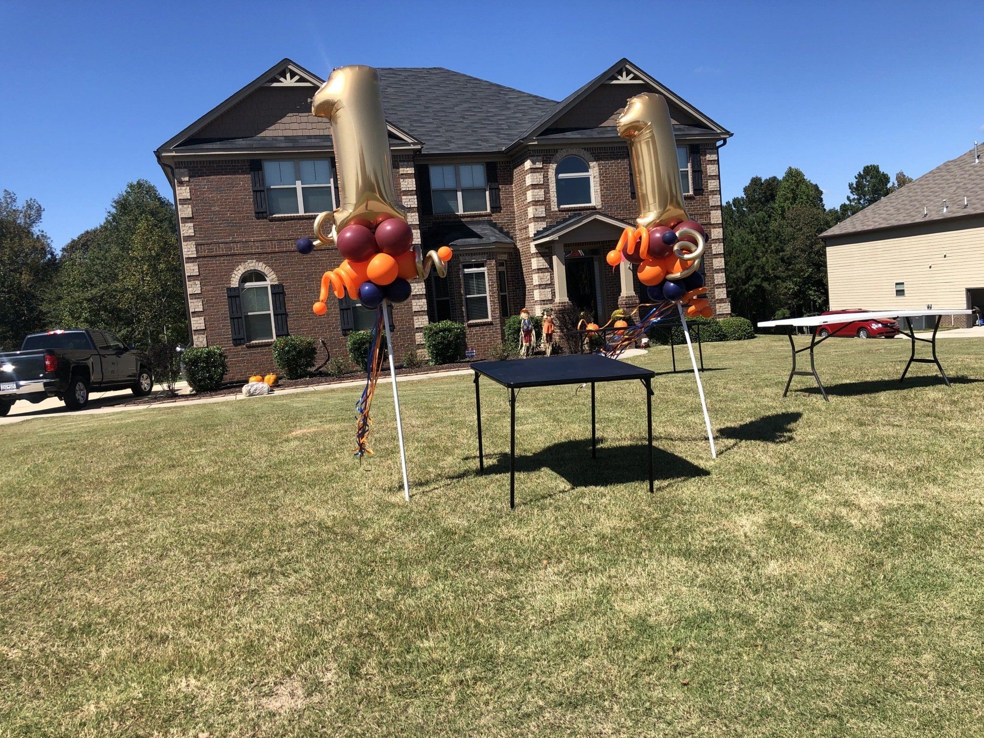 Large gold number one balloon yard display with balloon clusters for outdoor first birthday party at home