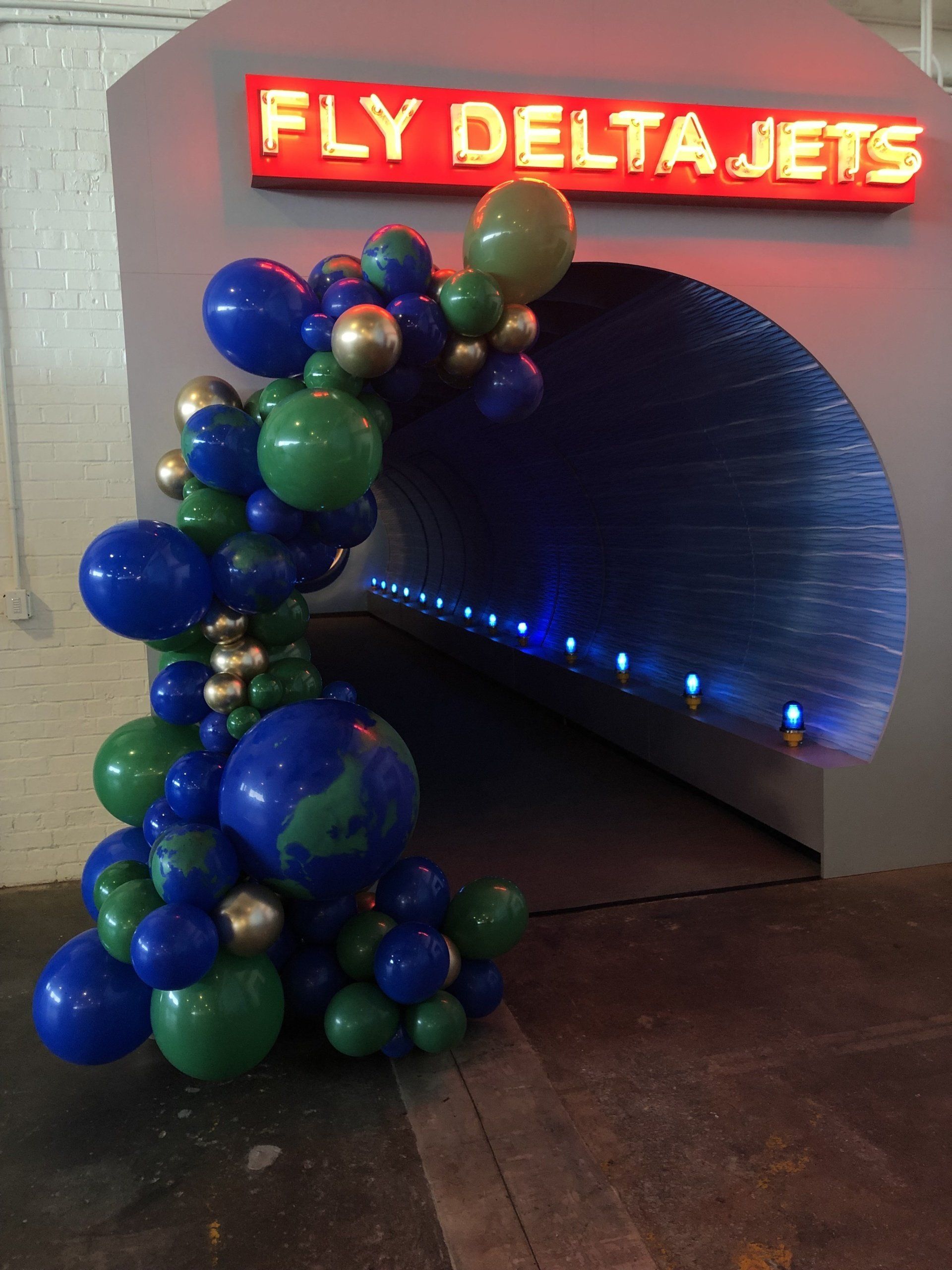 Blue and green balloon installation around neon sign entrance for corporate or themed event