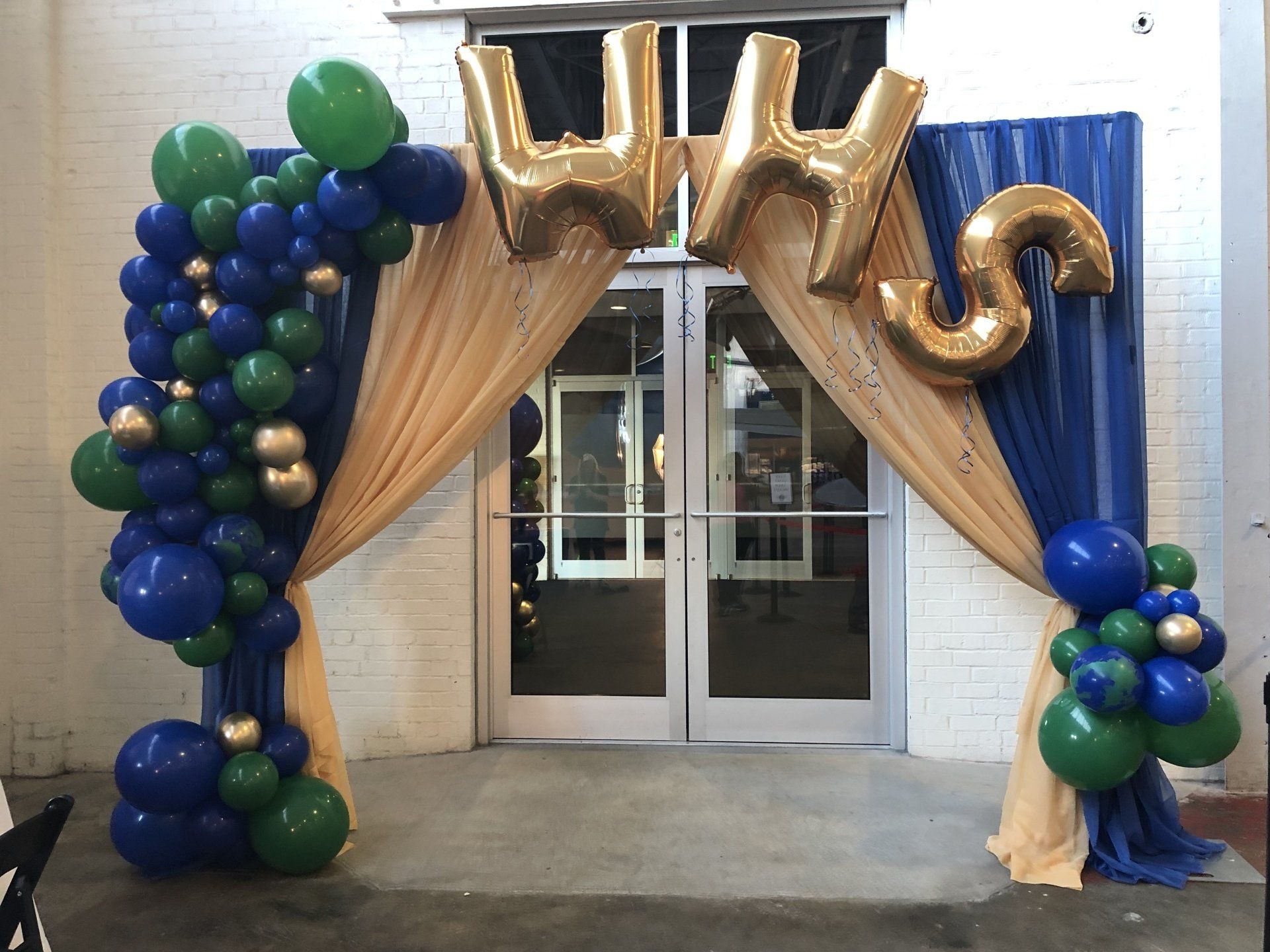 Blue green and gold balloon columns framing draped doorway with gold letter balloons for UWS event