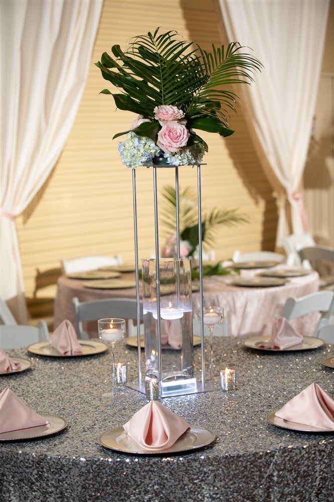 Tall tropical greenery centerpiece with roses and hydrangeas on a gold stand with draped backdrop