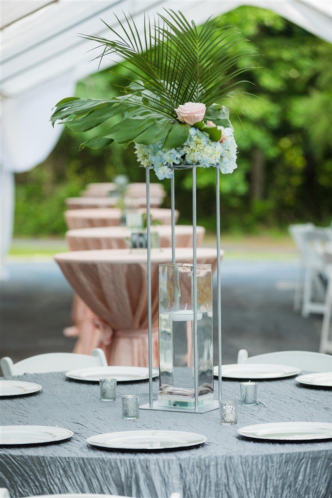 Tropical floral arrangement with palm leaves and hydrangeas displayed outdoors under a tent