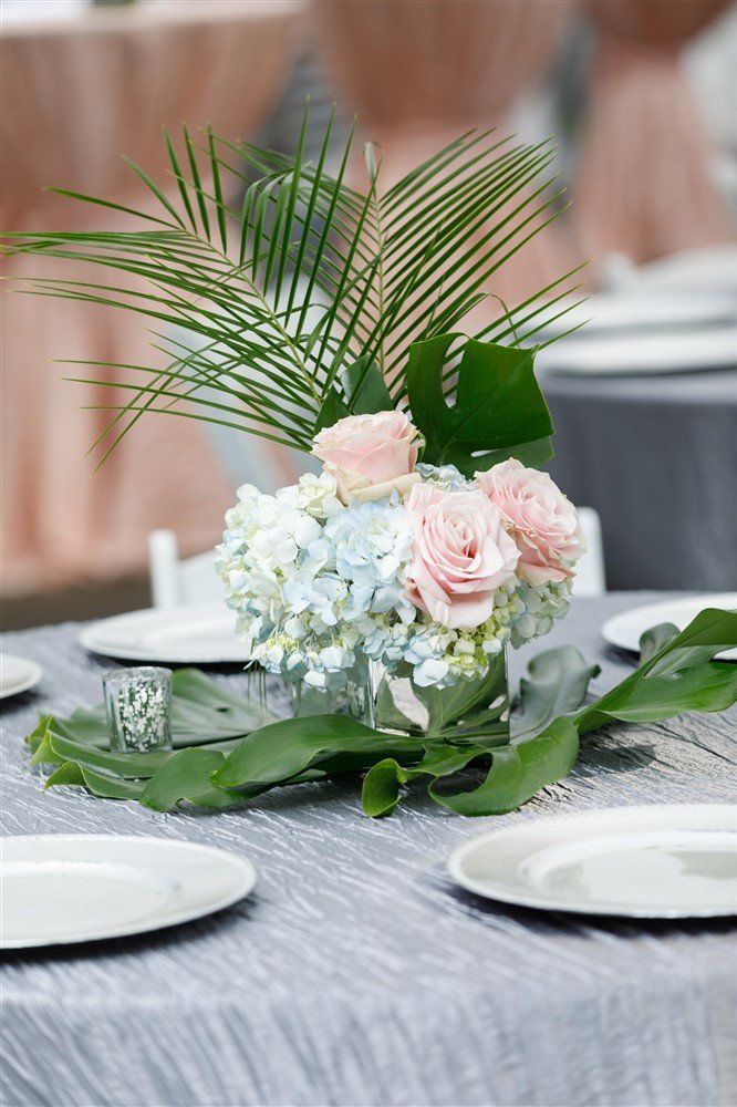 Close-up of palm fronds and greenery centerpiece with soft blush drapery in the background