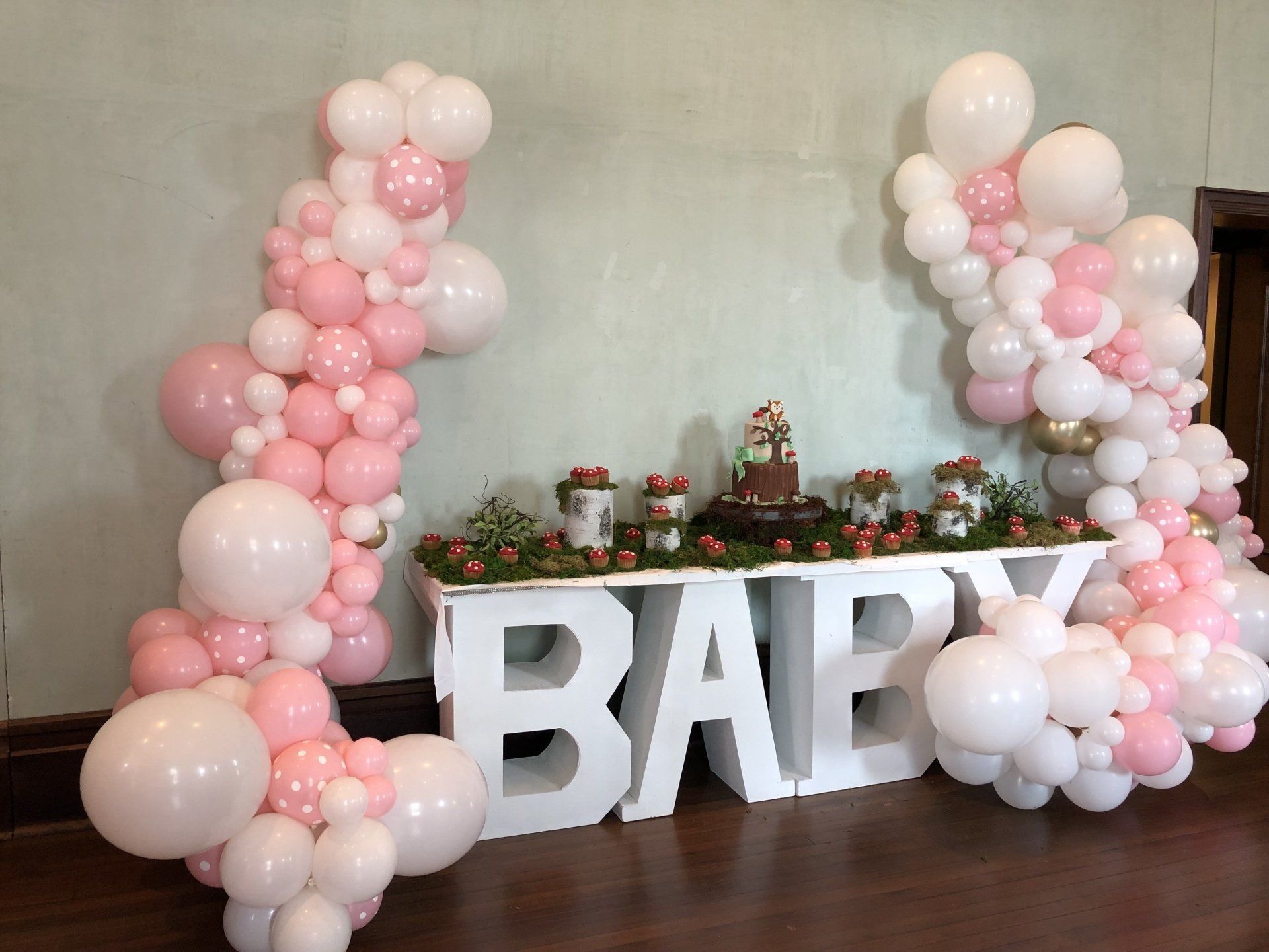 Pink and white baby shower balloon columns with marquee BABY letters and greenery table display