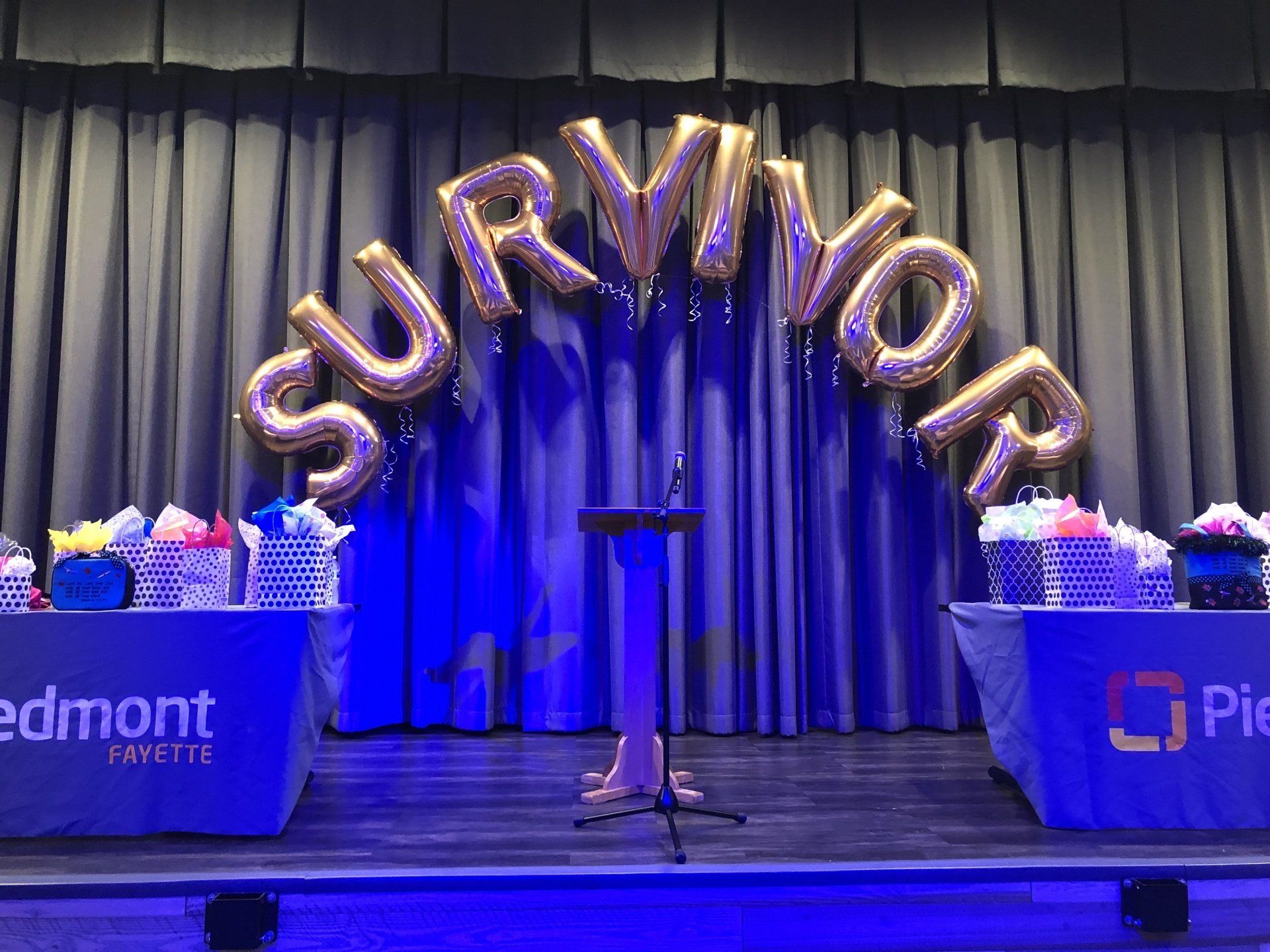 Gold survivor letter balloons on stage with blue lighting for cancer survivor celebration or awareness event decor