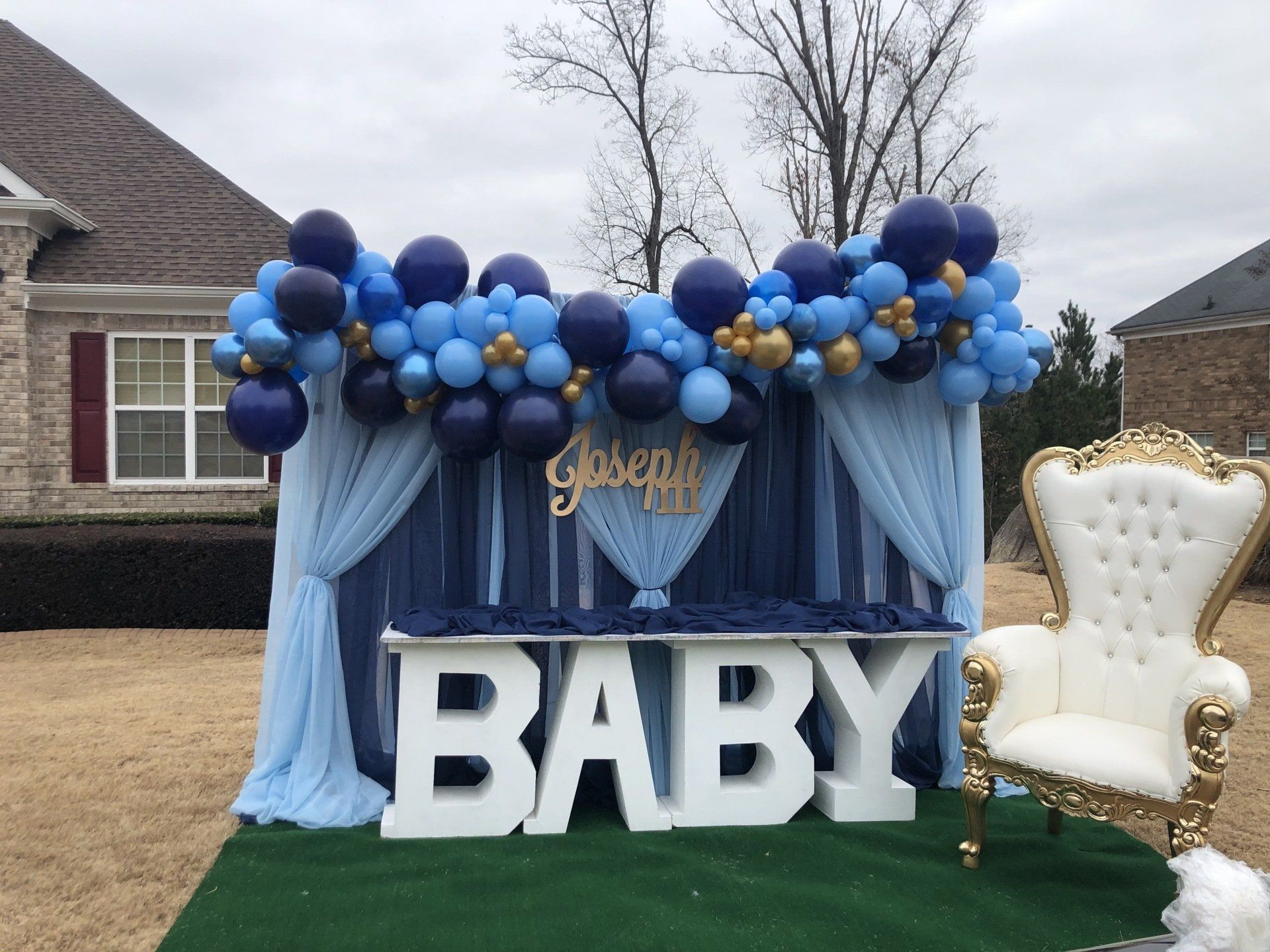 Blue and gold baby shower balloon backdrop with draped curtains marquee BABY letters and throne chair
