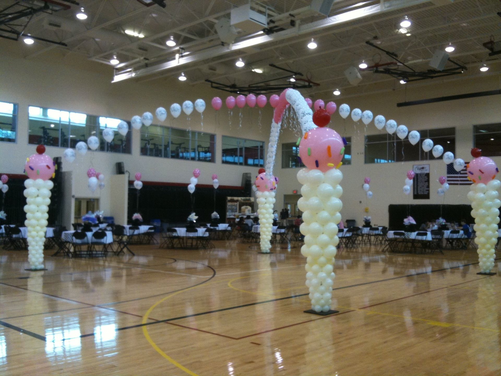 Two large balloon archways with primarily white and pink crisscrossed. 