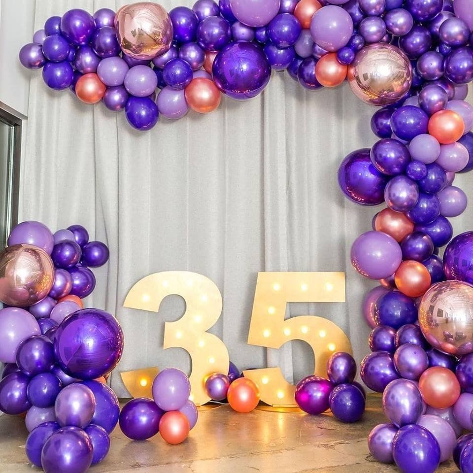 Purple lavender and rose gold balloon garland with chrome accents on white draped backdrop