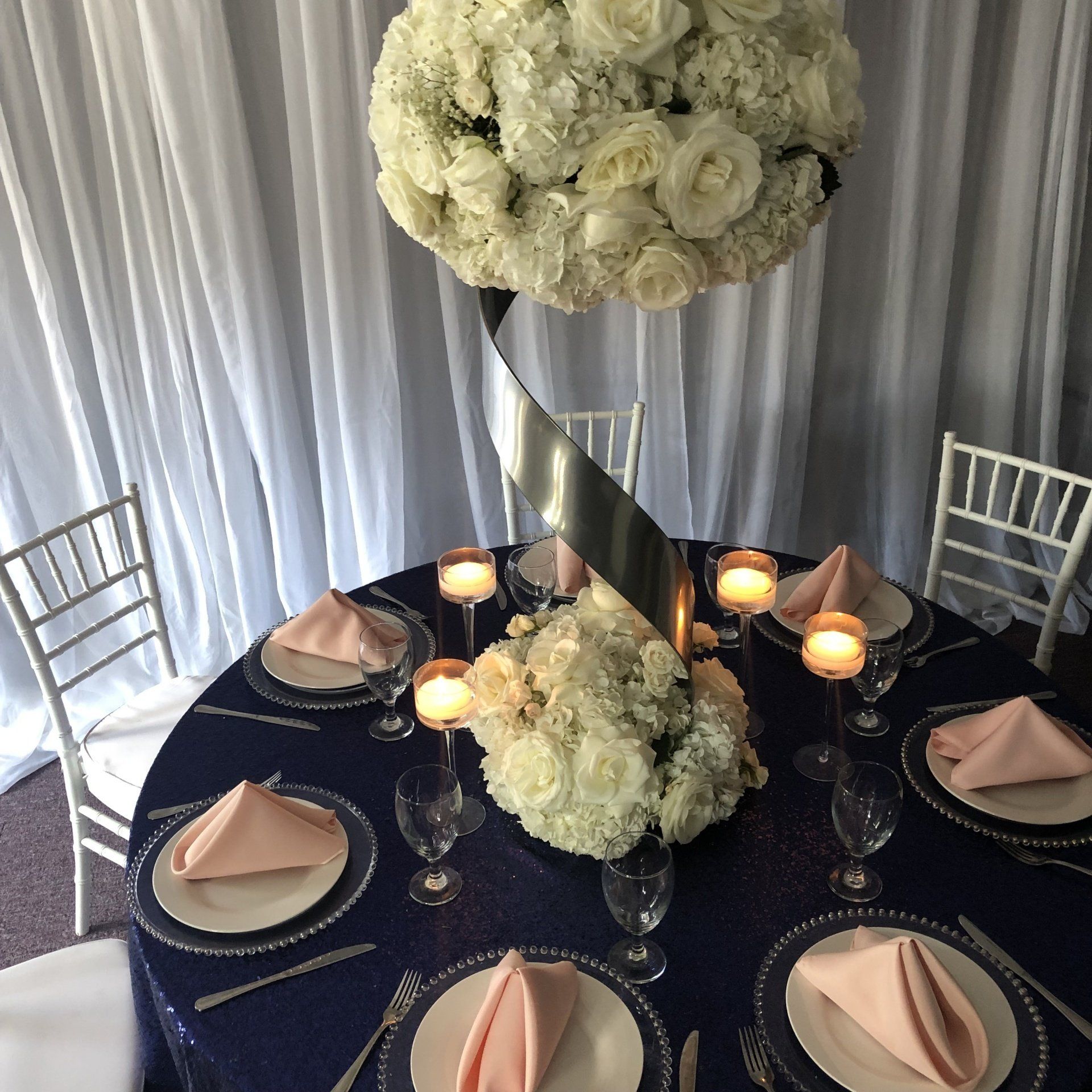 Large white floral ball centerpiece on a modern gold stand with candles and formal table setting
