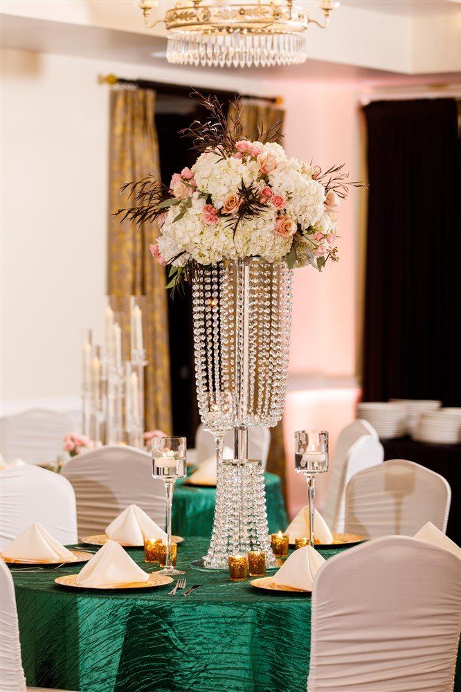 Tall blush and ivory floral centerpiece with roses and greenery in an elegant reception space