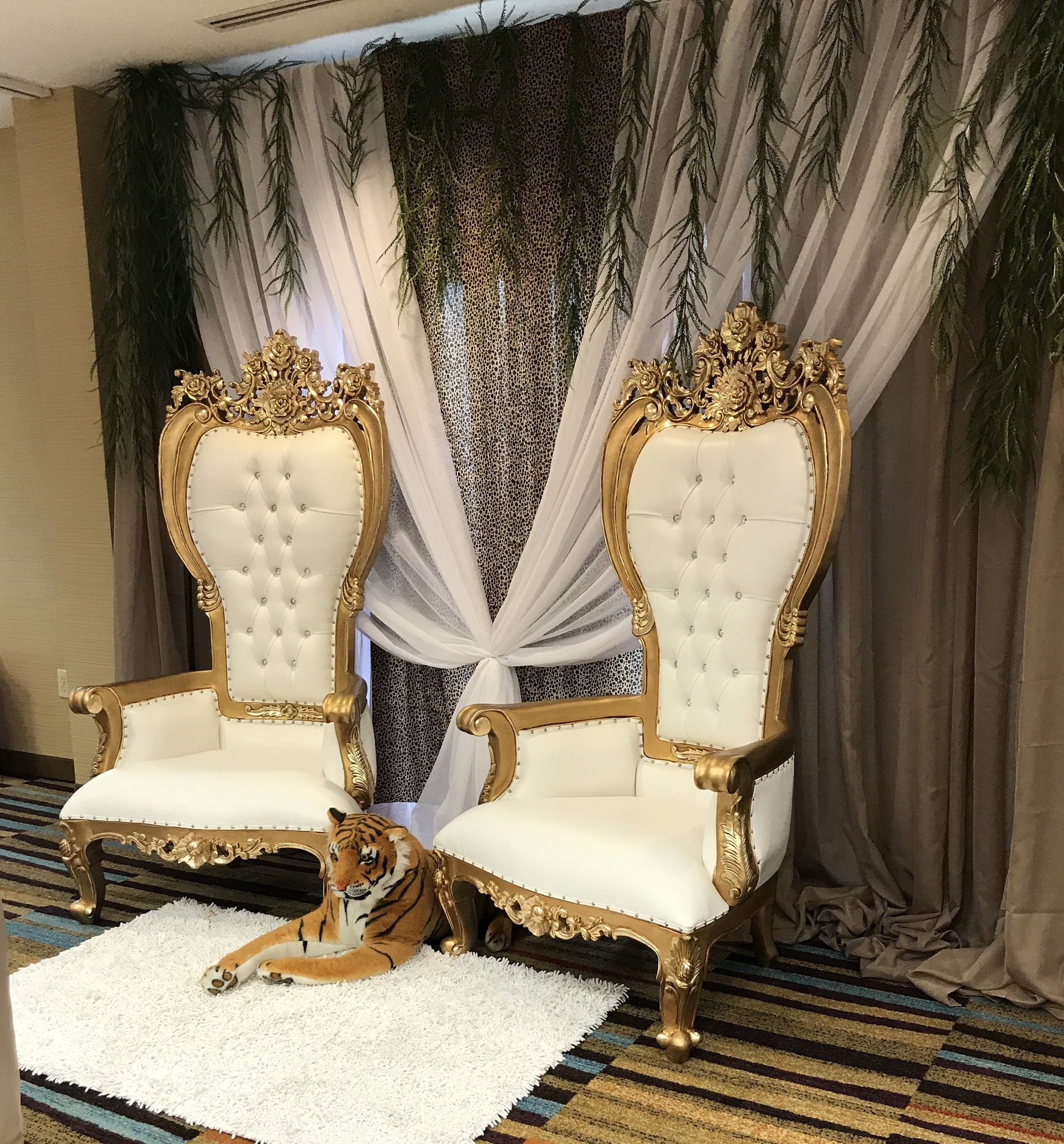 Gold and ivory throne chairs with greenery and white draped backdrop for elegant wedding setup