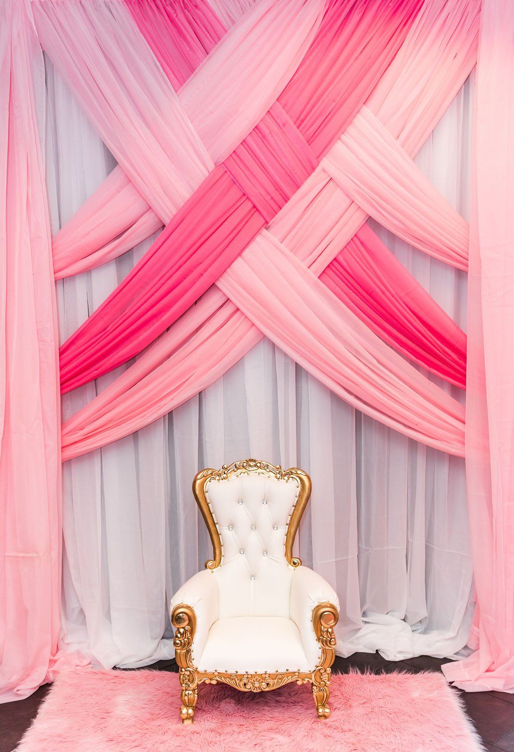 Kids gold trimmed throne on a pink rug with draping in a criss cross design in the background.