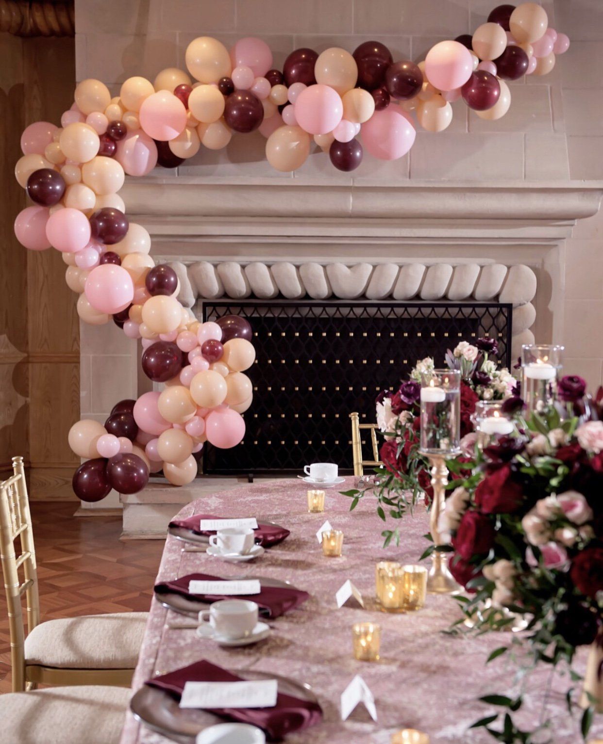A pink and red balloon garland is wrapped around a stately fireplace.