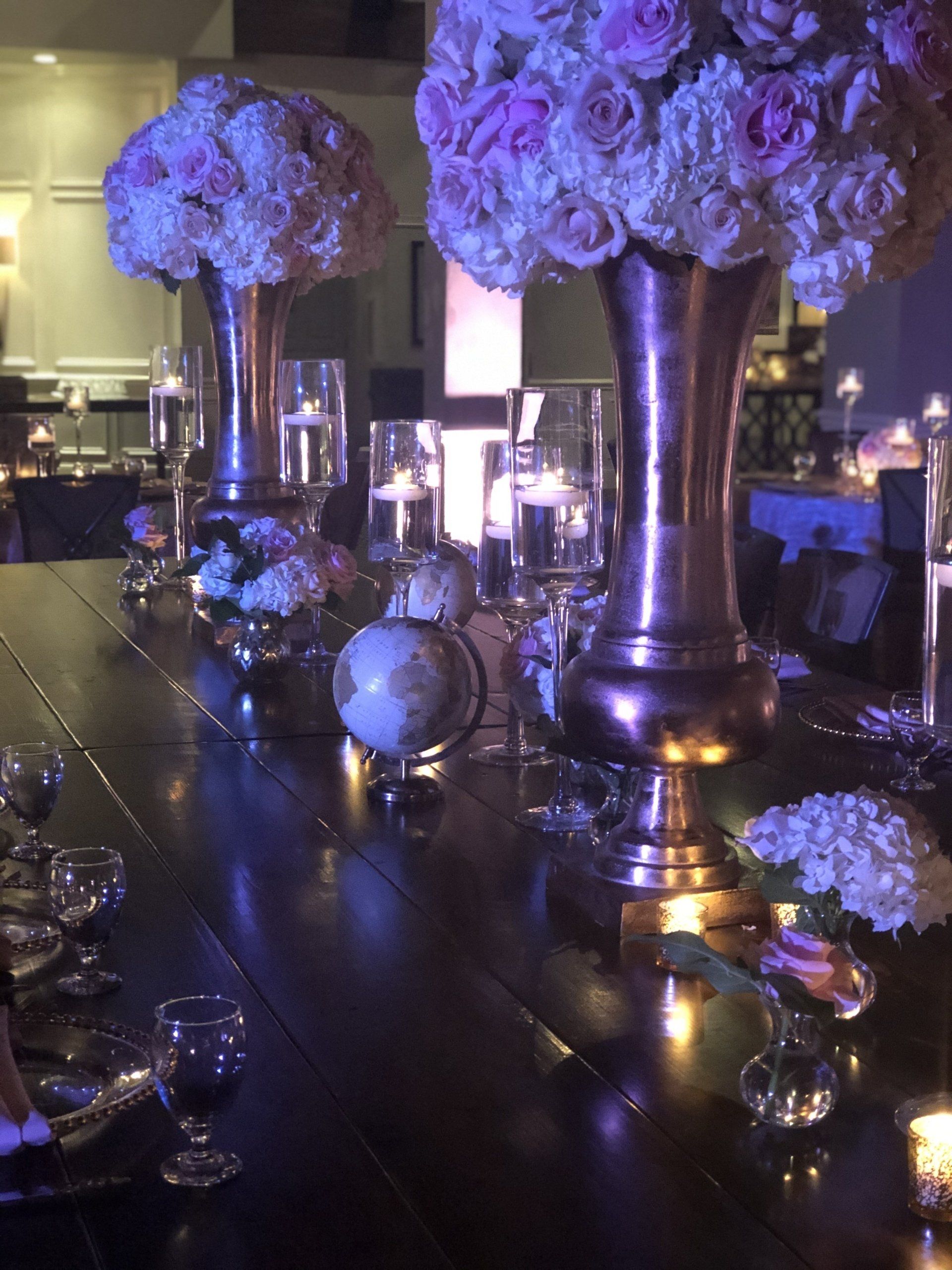 Purple floral centerpieces in tall vases with candles for formal event décor